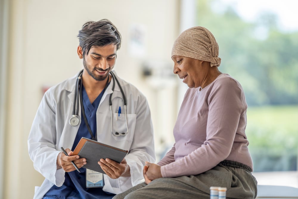 Male doctor reviewing chart with older female patient wearing a scarf on her head.