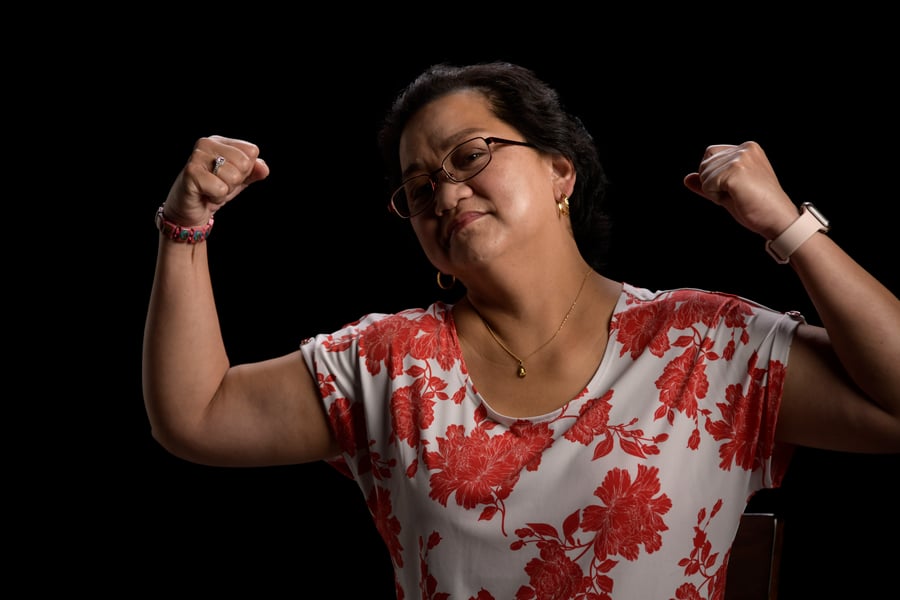 A woman in a floral top looks at the camera and flexes her biceps