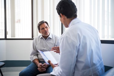 A male doctor holding a pamphlet and talking with a senior patient in a medical office.