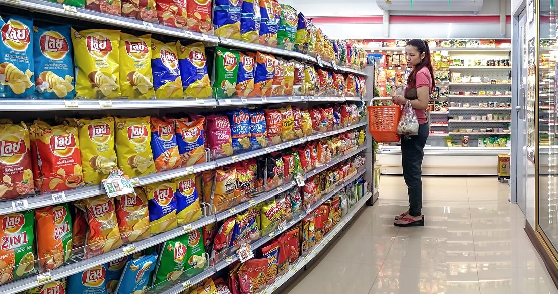 A woman holds a shopping basket and shops in the potato chips section of a grocery store