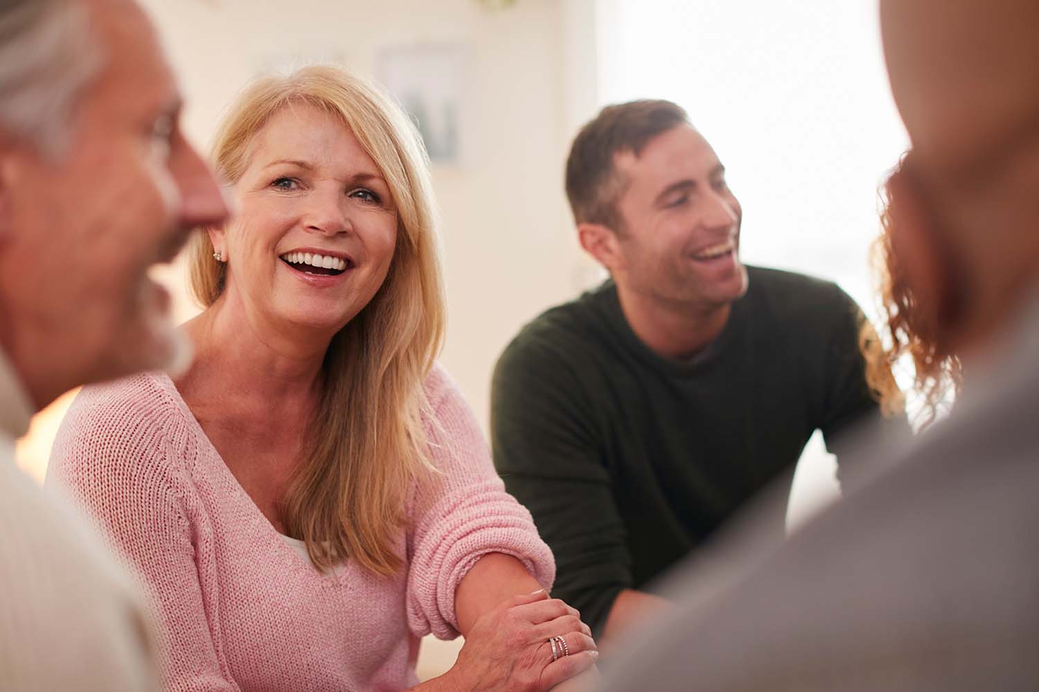 A group of people talking and smiling. In the center is a blonde woman in a pink sweater.