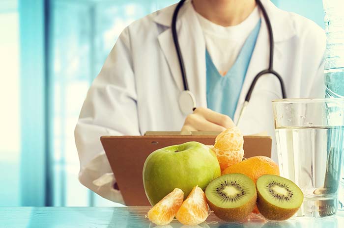 médico de pie detrás de un montón de fruta y un vaso de agua