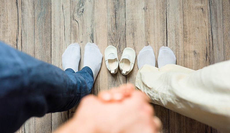 dos adultos cogidos de la mano con los zapatos de un niño pequeño entre ellos