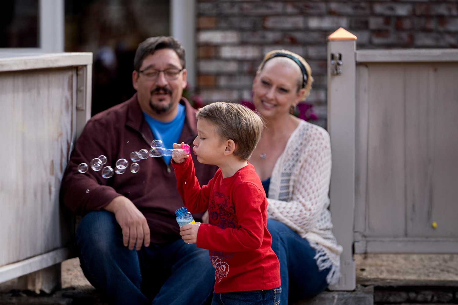 A young boy blows bubbles while his parents watch on and smile.